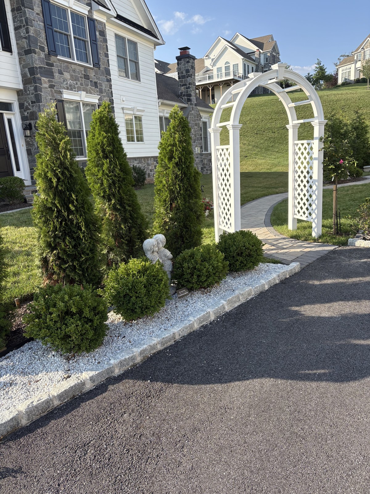 White garden arbor over a paver walkway framed by manicured shrubs and evergreens