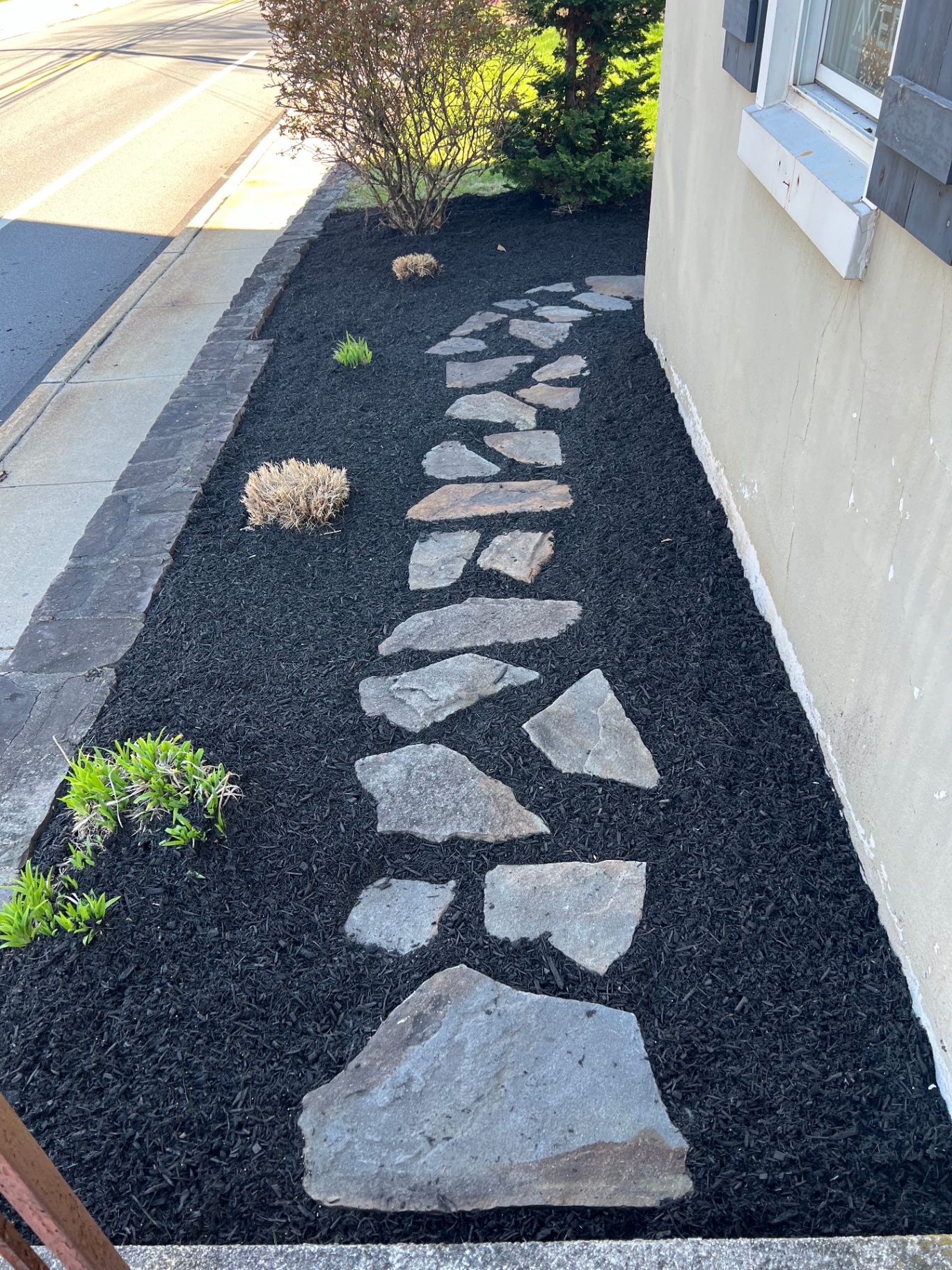 Flagstone stepping-stone path set in fresh black mulch alongside a home